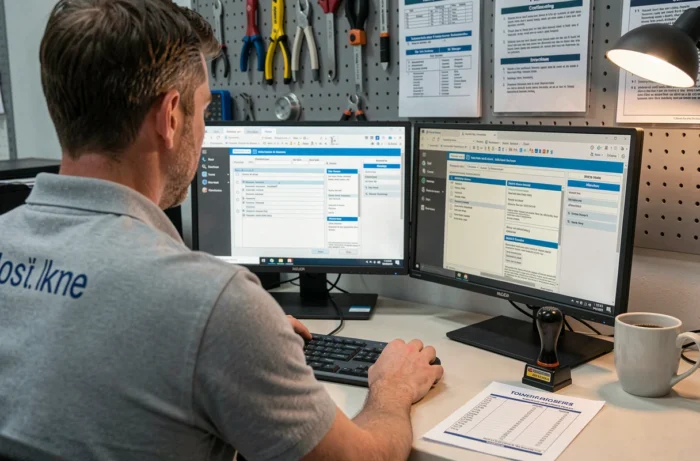 Inspecteur automobile en arrière-bureau gérant des documents de certification sur un double écran dans un espace affilié de contrôle technique